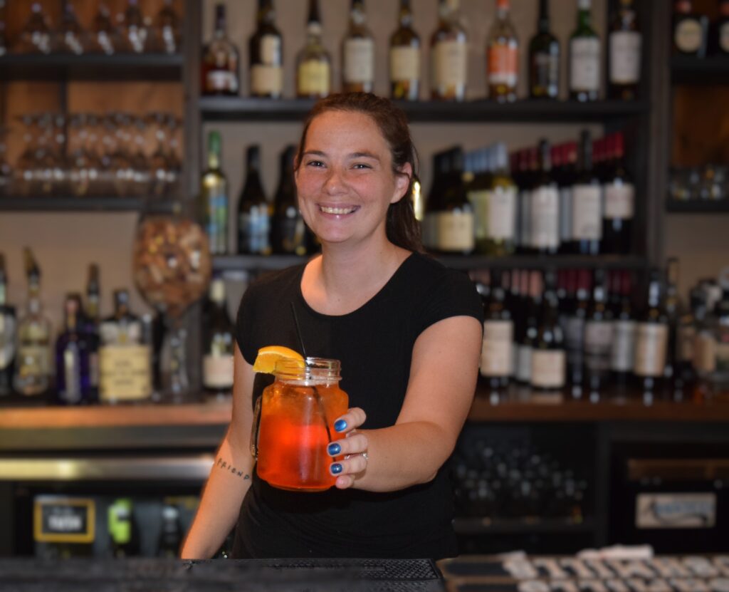 woman holding up a drink behind the bar