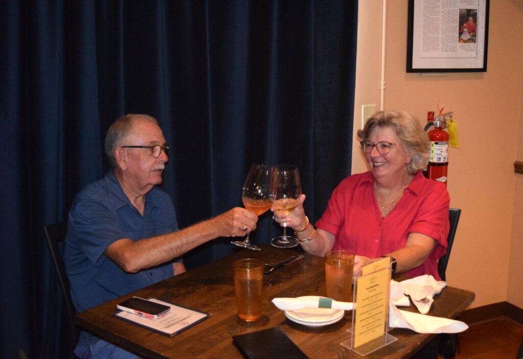 old woman in pink drinking wine with old man in blue shirt